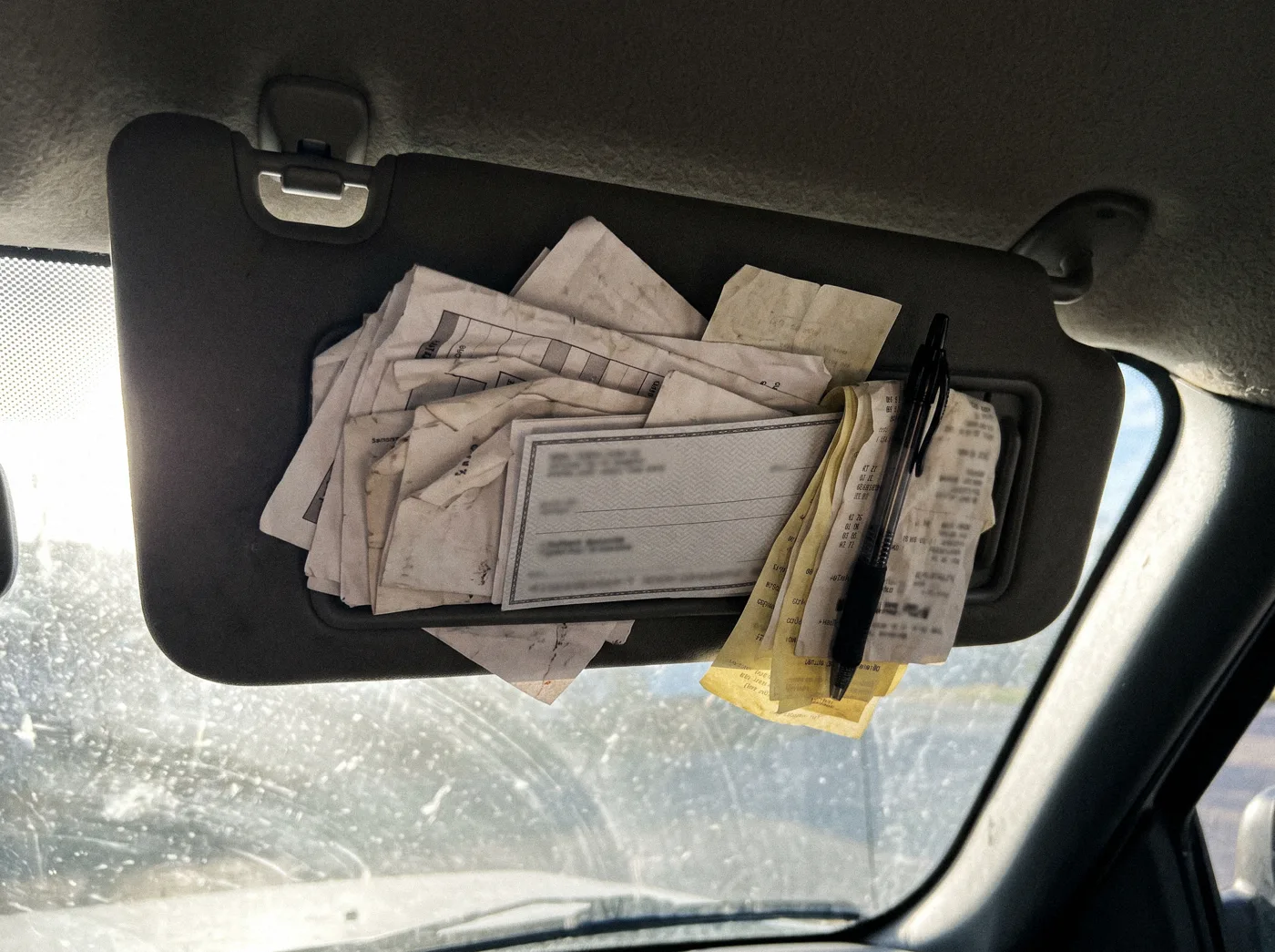 A truck sun visor stuffed with folded paper invoices, a check, and receipts