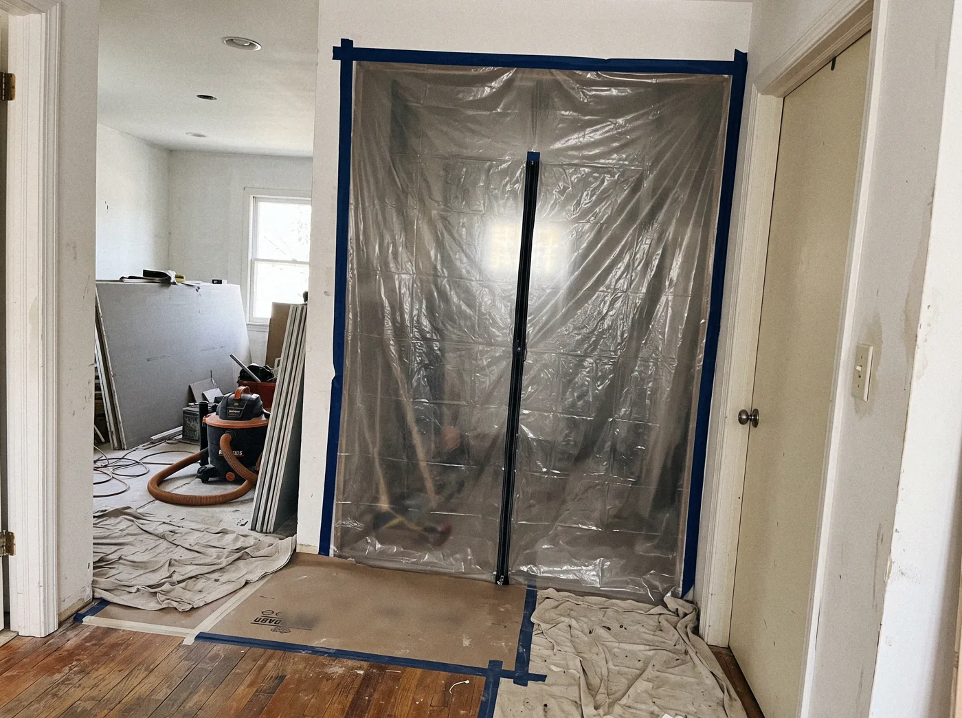 A plastic dust barrier with a zipper door across a hallway during a remodel, floors covered